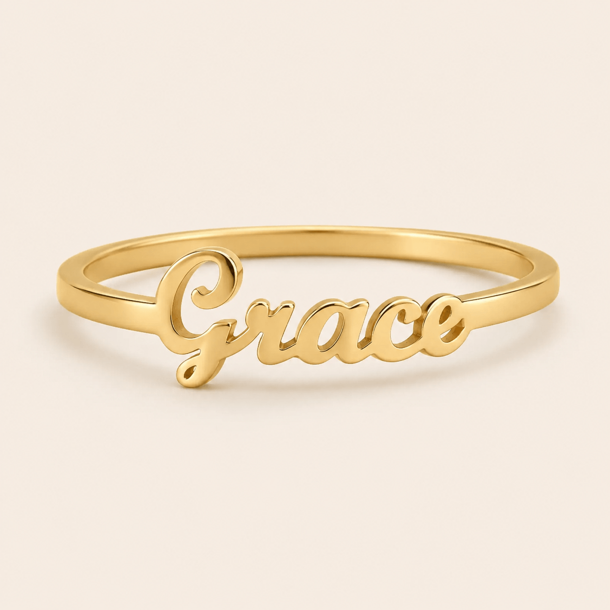 A gold name ring featuring the cursive script name 'Grace' on a smooth, polished band, set against a solid light beige background. at shine gold and diamonds