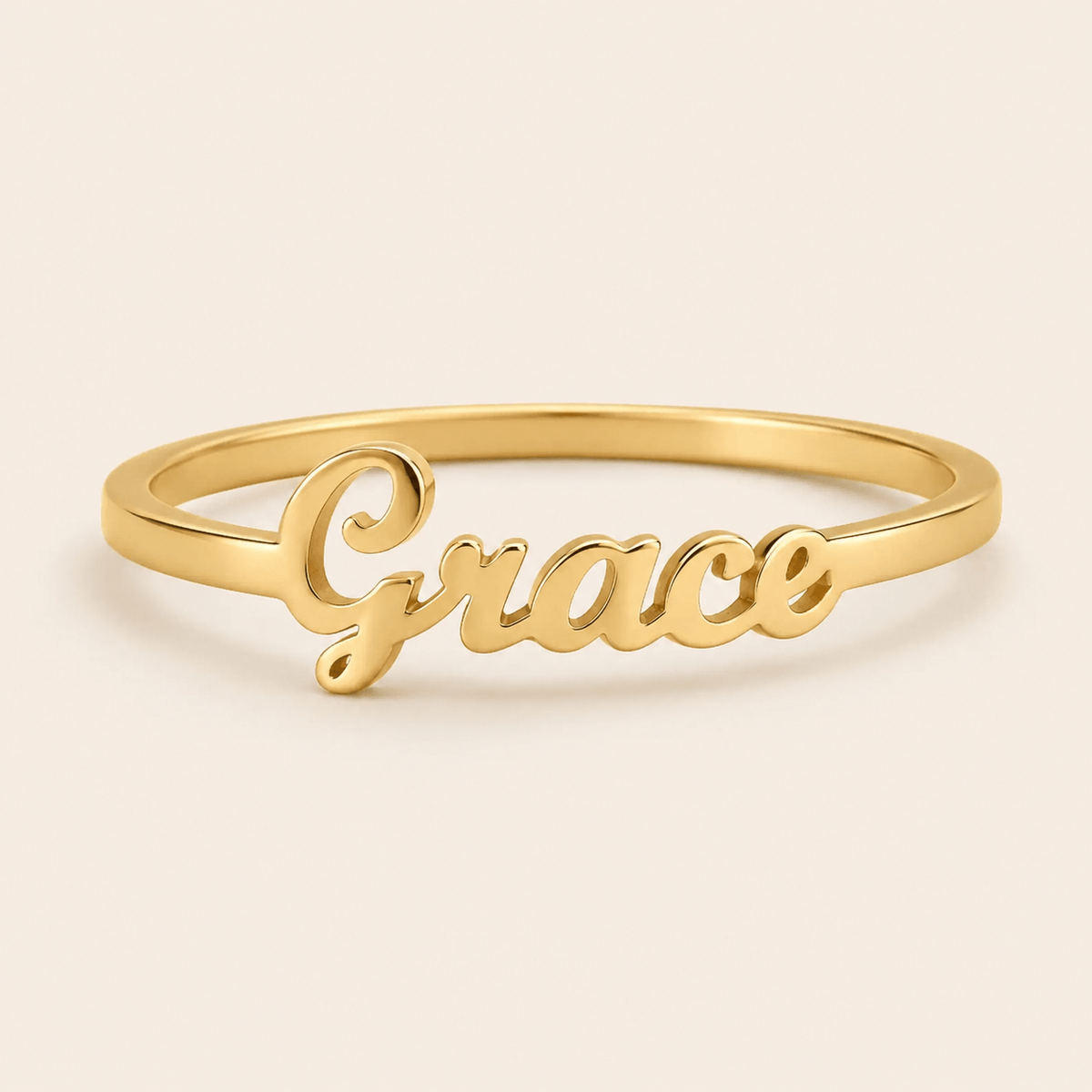 A gold name ring featuring the cursive script name 'Grace' on a smooth, polished band, set against a solid light beige background. at shine gold and diamonds